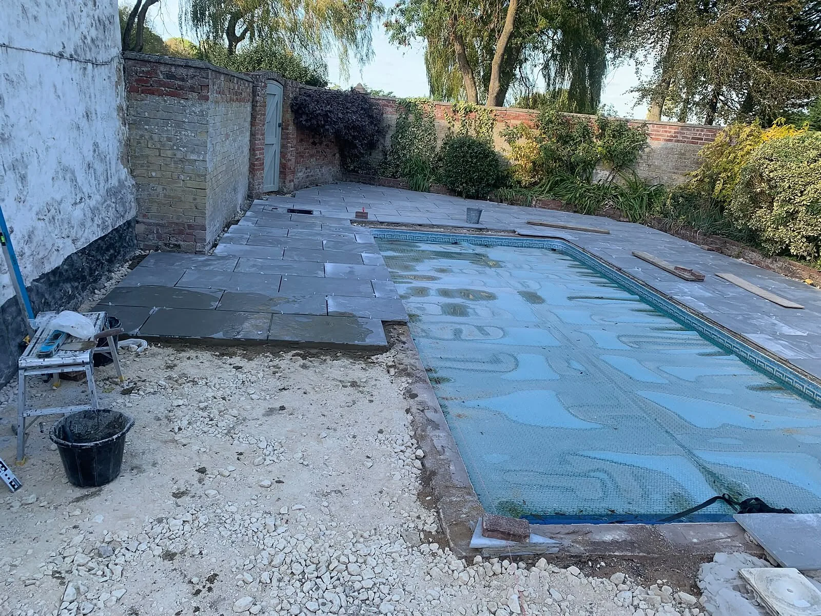 Grey paving being laid around a garden swimming pool – Fines Landscaping, West Norfolk